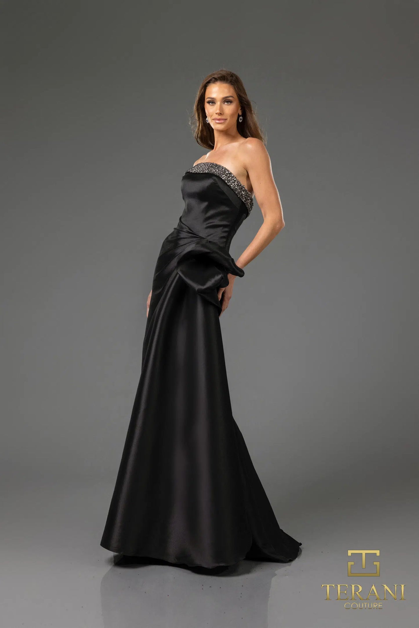 Terani 252E5131 strapless gown with embellished bodice, draped bow detail, and side slit, perfect for formal evenings and mother of the bride or groom.  The model is wearing the dress in the color black.