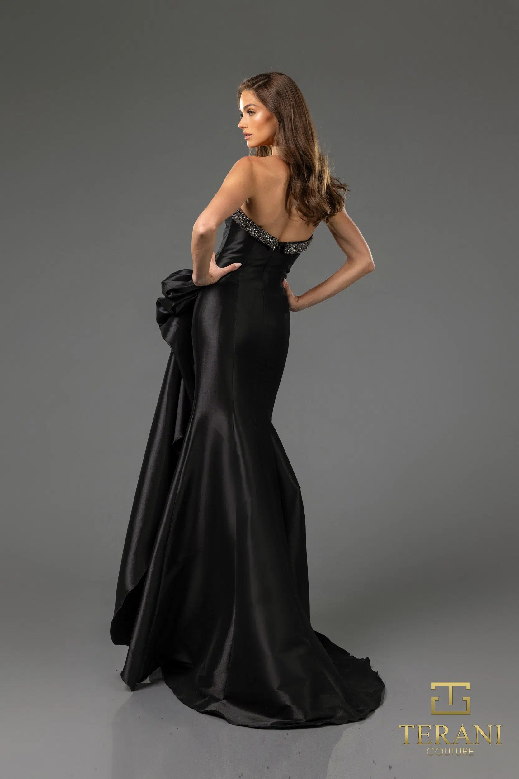 Terani 252E5131 strapless gown with embellished bodice, draped bow detail, and side slit, perfect for formal evenings and mother of the bride or groom.  The model is wearing the dress in the color black.