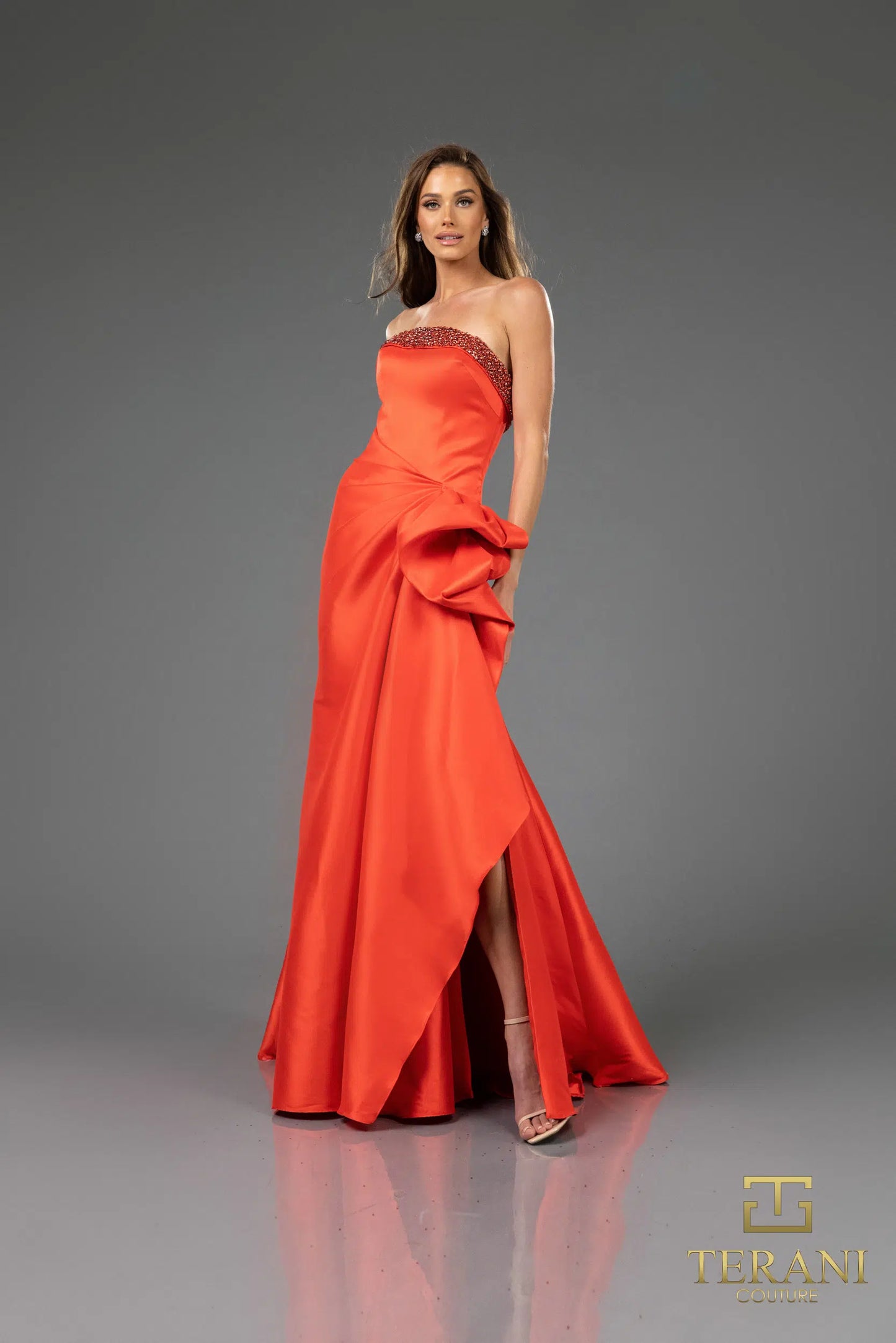 Terani 252E5131 strapless gown with embellished bodice, draped bow detail, and side slit, perfect for formal evenings and mother of the bride or groom.  The model is wearing the dress in the color Red.