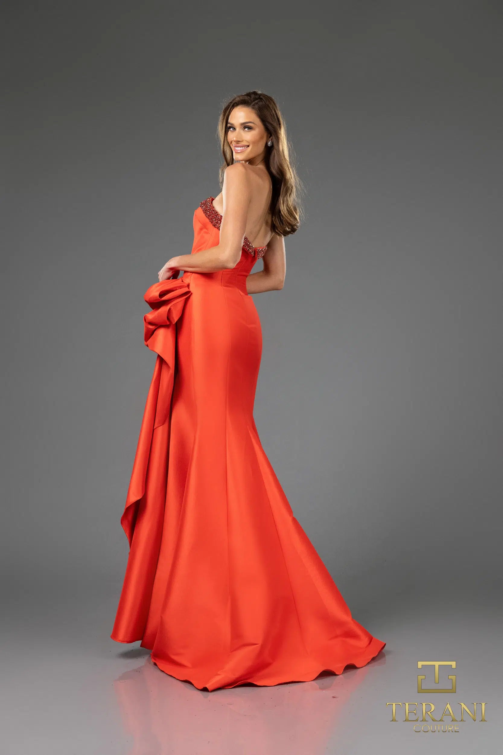 Terani 252E5131 strapless gown with embellished bodice, draped bow detail, and side slit, perfect for formal evenings and mother of the bride or groom.  The model is wearing the dress in the color Red.